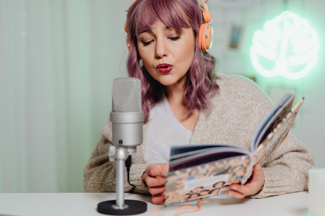 Frau mit rosa Haaren und Buch spricht in ein Mikro