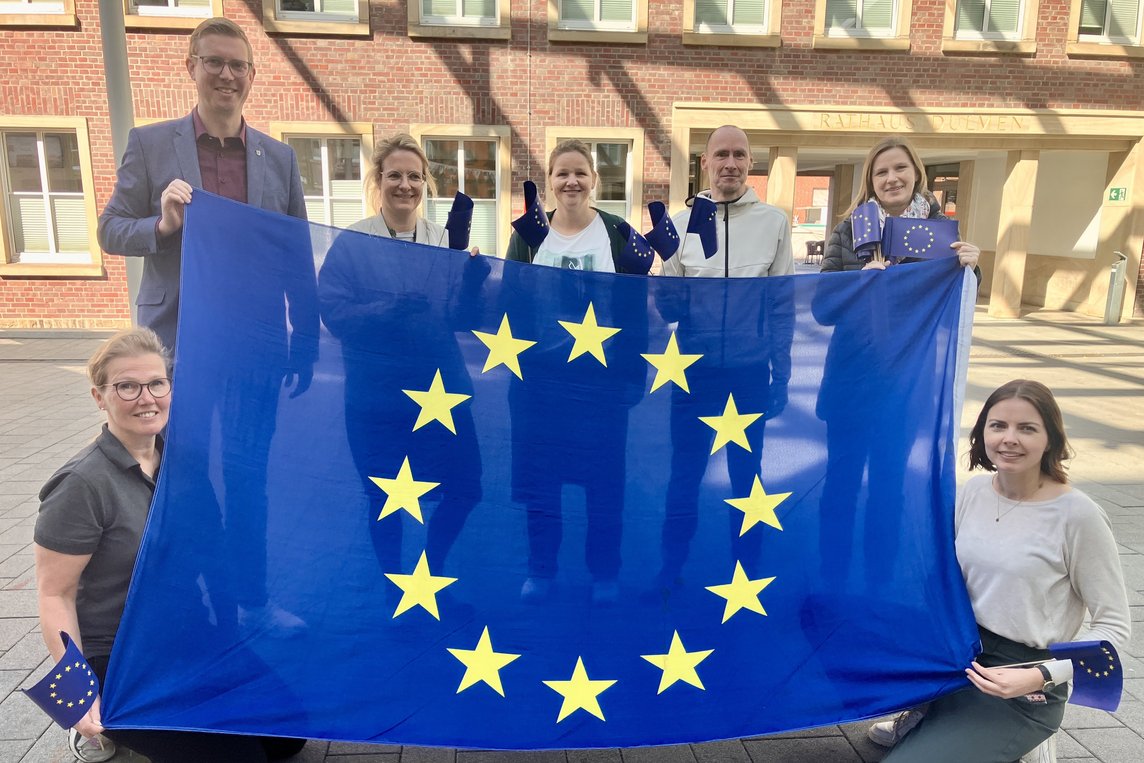 Laden gemeinsam zur Dülmener Europa-Woche mit vielen Veranstaltungen ein (v. re.): Melanie Hölker von der Stadt Dülmen, Pako-Vorsitzende Eva Vasmer, Stadtarchivar Dr. Stefan Sudmann, Bücherei-Leiterin Petra Toppmöller, VHS-Leiterin Dr. Marie Hologa, Bürgermeister Carsten Hövekamp und Katja Escher vom Bistro Orange. Foto: Stadt Dülmen/Siemes